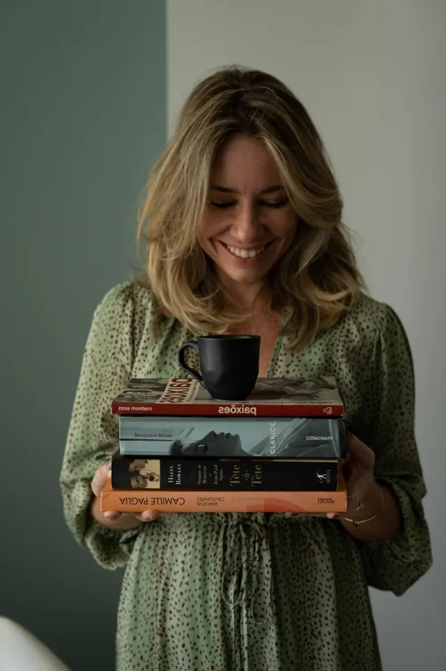 Milena Alves de Carvalho sorrindo, com uma pilha de livros e uma xícara nas mãos